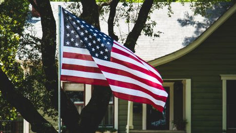 American flag flying on a pole in front of a tree outside of a house.