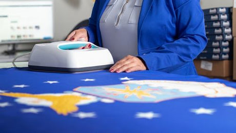 A blue flag with white stars and gold accents being ironed on a table by a woman