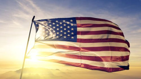 An American flag flying on a flagpole with rays of sunlight shining through