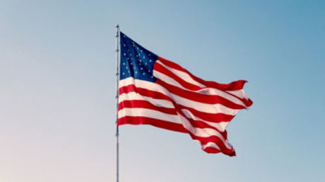 An American flag flying on a flagpole under a blue sky