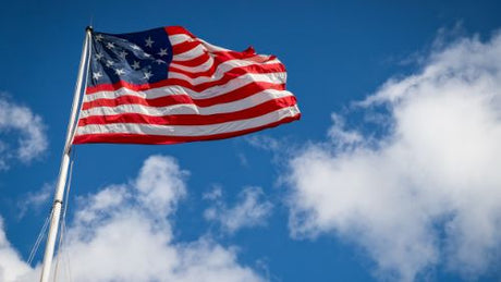 An American flag flying on a flagpole under a blue sky with clouds