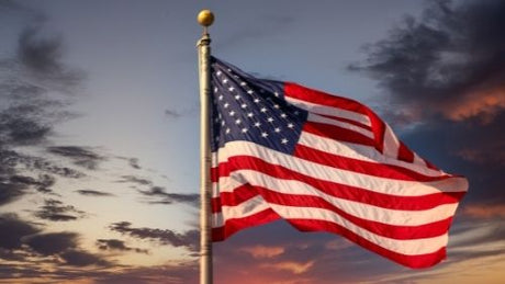 An American flag flying on a flagpole under a dark gray and blue sky