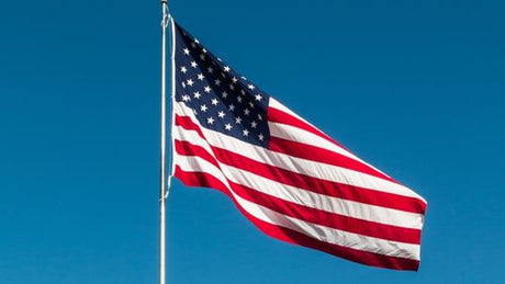 An American flag flying on a flagpole under a blue sky