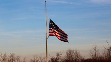 American flag flying at half-mast on an outdoor flagpole, symbolizing national mourning and remembrance.